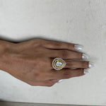 A close-up of a hand with silver manicured nails wearing a gold ring featuring a teardrop-shaped clear gemstone surrounded by a halo of small clear stones.