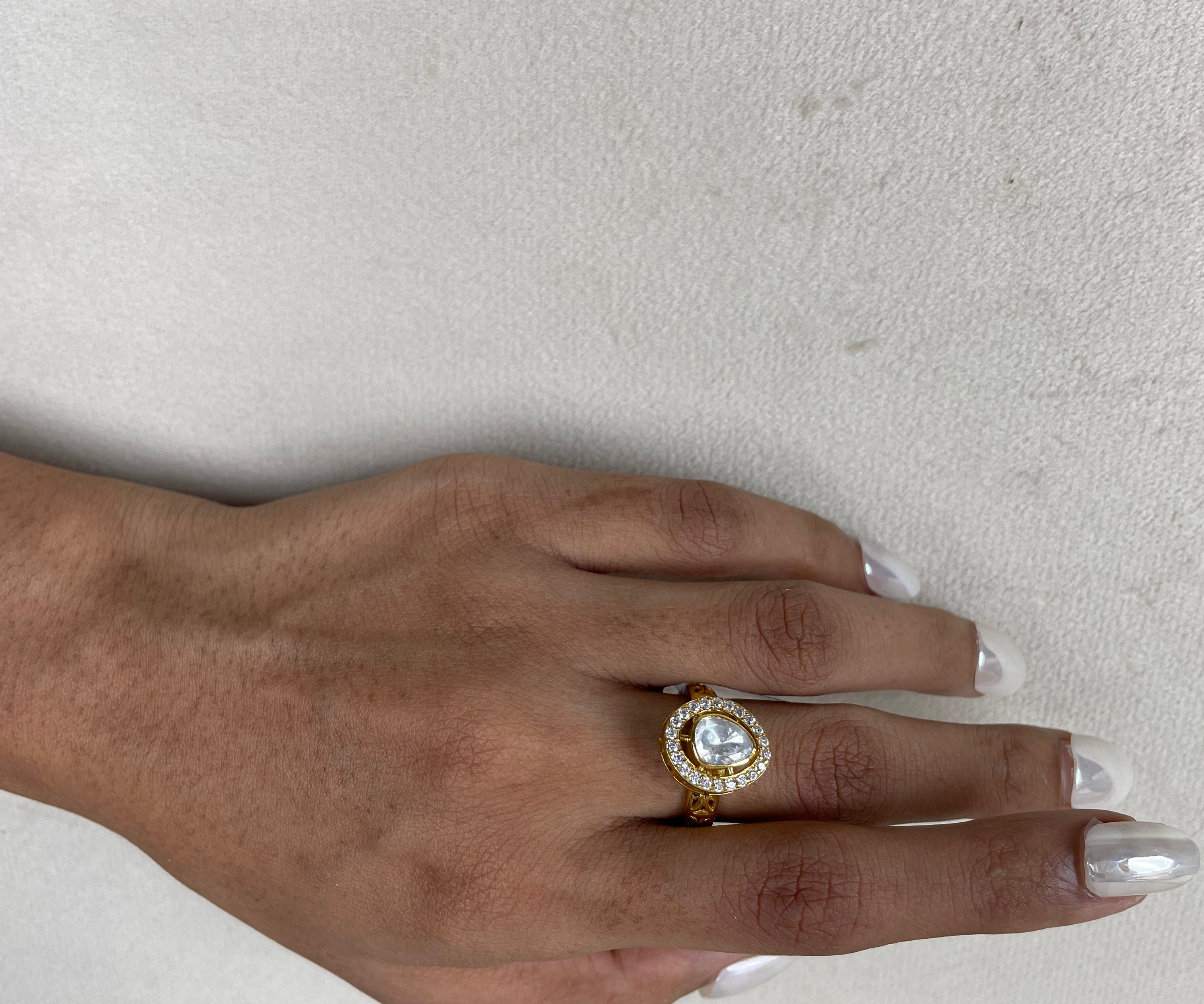 A silver gold-plated ring with a large clear teardrop-shaped gemstone surrounded by small clear stones, worn on a person's finger against a light textured background.