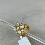 A gold-plated ring with multiple clear teardrop-shaped stones, resting on a clear glass rod with a white product tag attached, set against a neutral gray background.