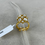 A gold ring with a floral cluster of clear stones, displayed on a clear plastic stand over a textured gray surface.