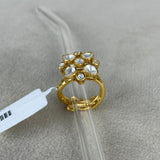 A gold ring with a floral cluster of clear stones, displayed on a clear plastic stand over a textured gray surface.