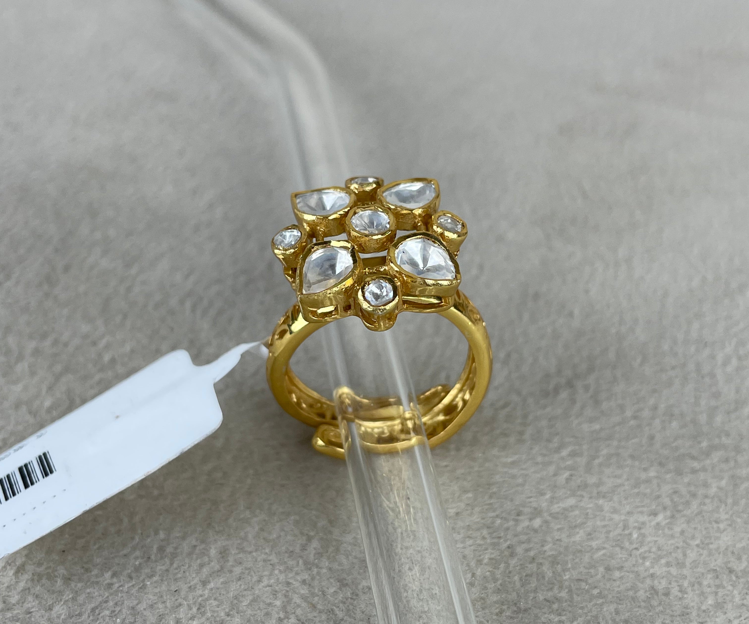 A gold ring with a floral cluster of clear stones, displayed on a clear plastic stand over a textured gray surface.