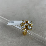 A gold ring with a cluster of clear heart-shaped and round stones, displayed on a clear glass rod over a textured light gray background.
