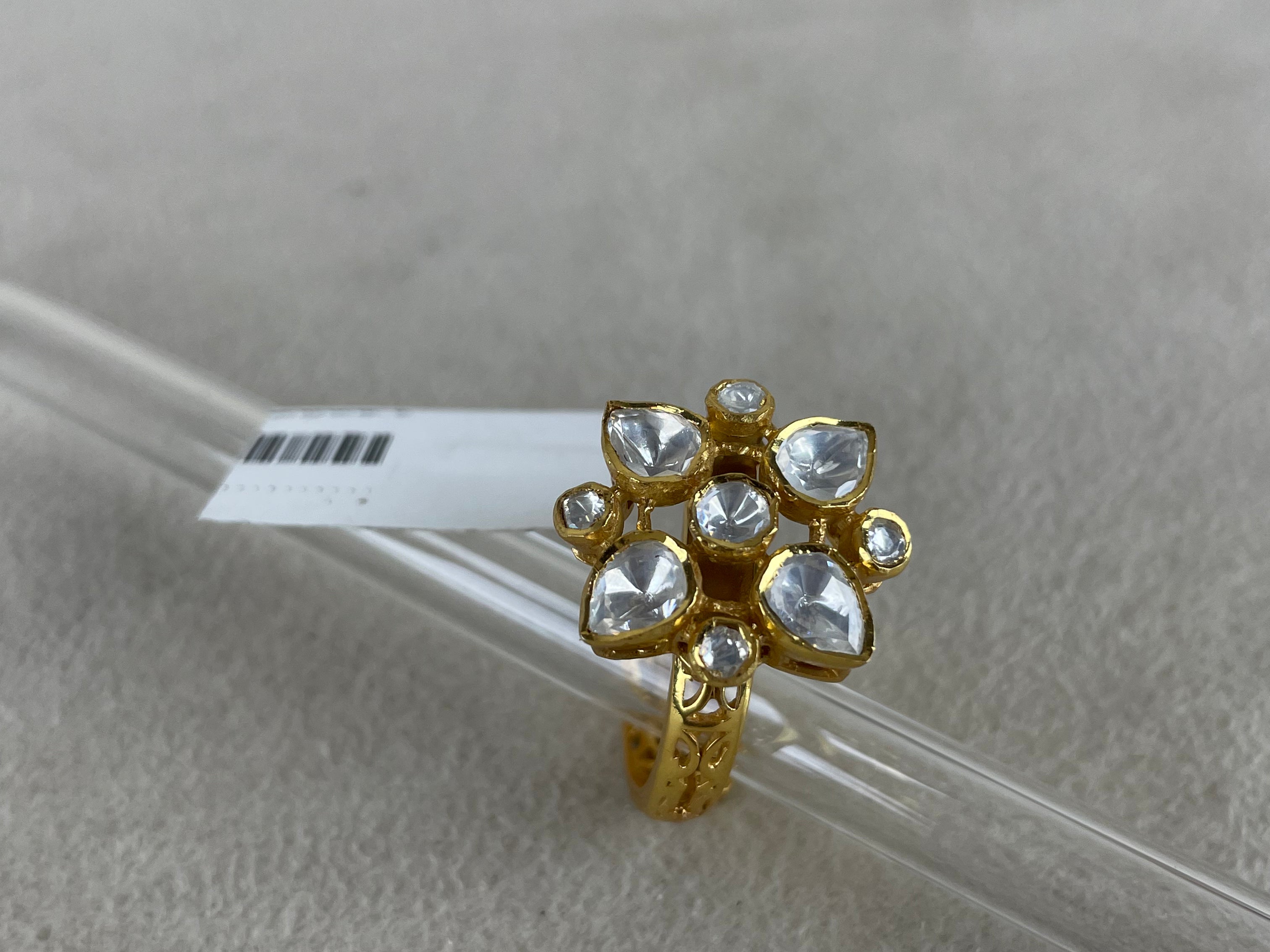 A gold ring with a cluster of clear heart-shaped and round stones, displayed on a clear glass rod over a textured light gray background.