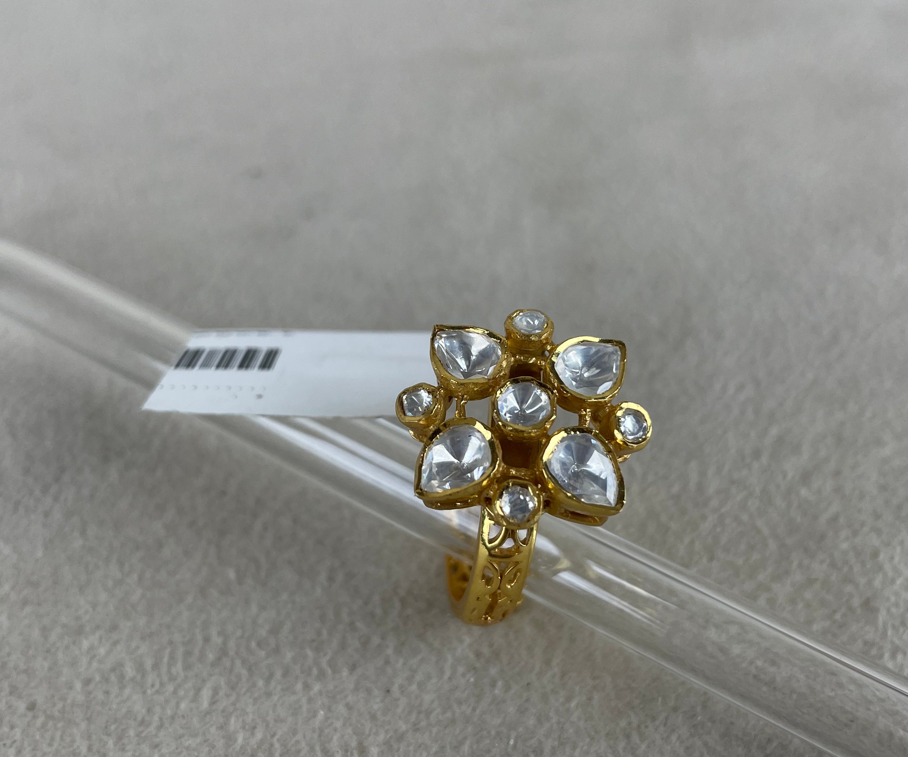 A gold ring with a cluster of clear heart-shaped and round stones, displayed on a clear glass rod over a textured light gray background.
