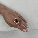 A gold-plated ring with a large green oval stone, a red rectangular stone, and white stones on a hand.