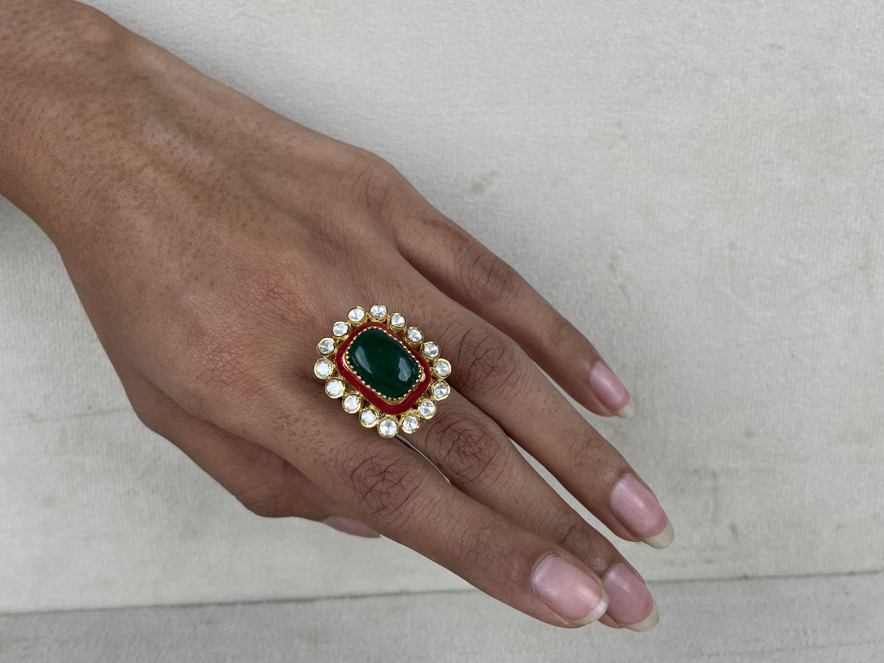 A gold-plated ring with a large green oval stone, a red rectangular stone, and white stones on a hand.