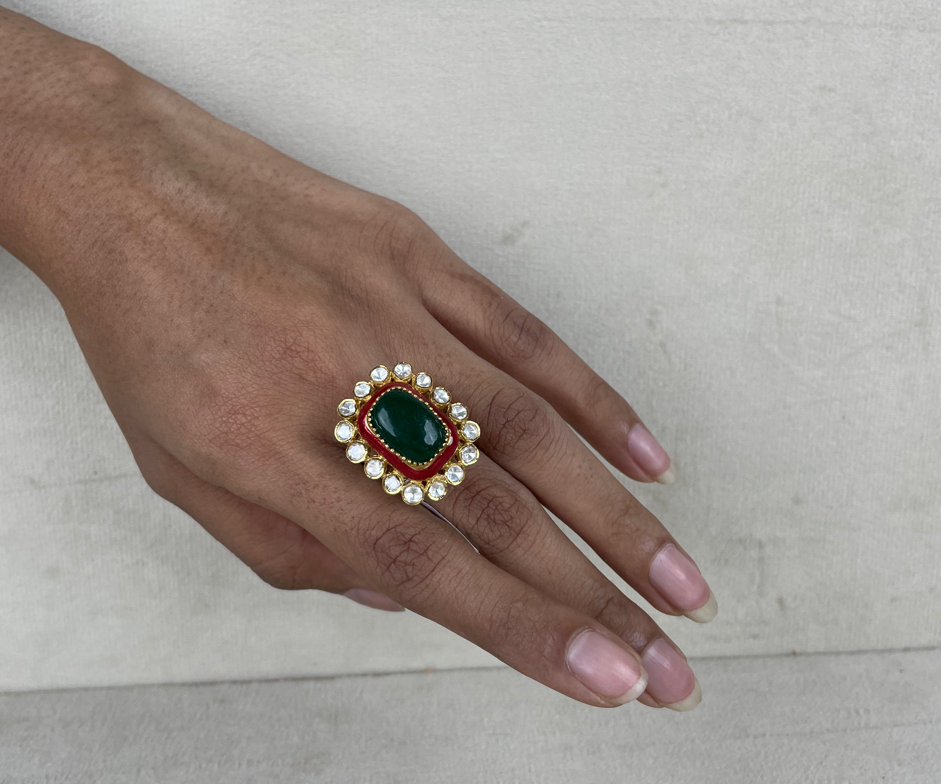 A gold-plated ring with a large green oval stone, a red rectangular stone, and white stones on a hand.