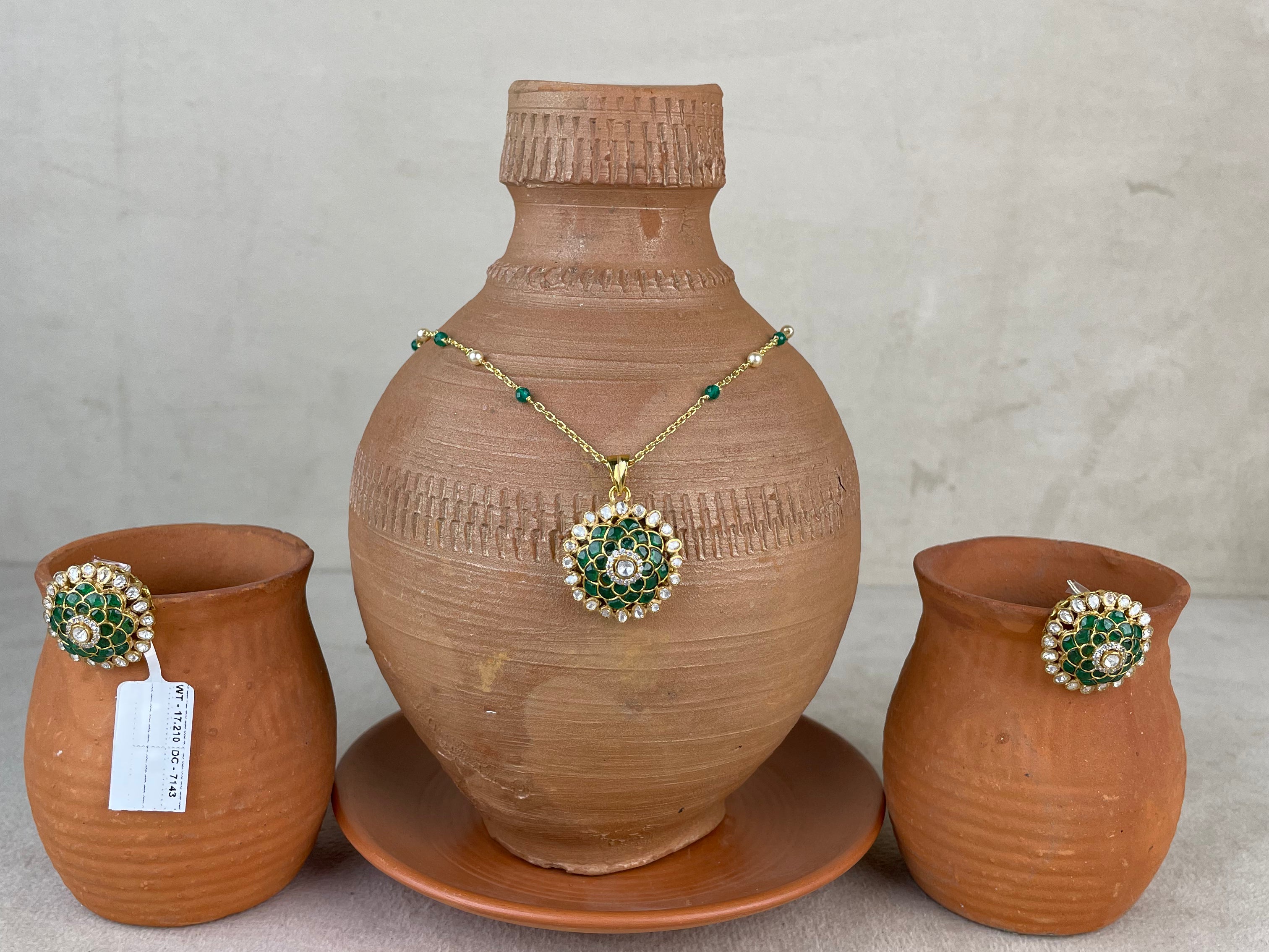 A terracotta clay set featuring a large decorative vase on a matching saucer, flanked by two smaller clay pots, with a gold-tone necklace and matching brooch displayed on the vase.
