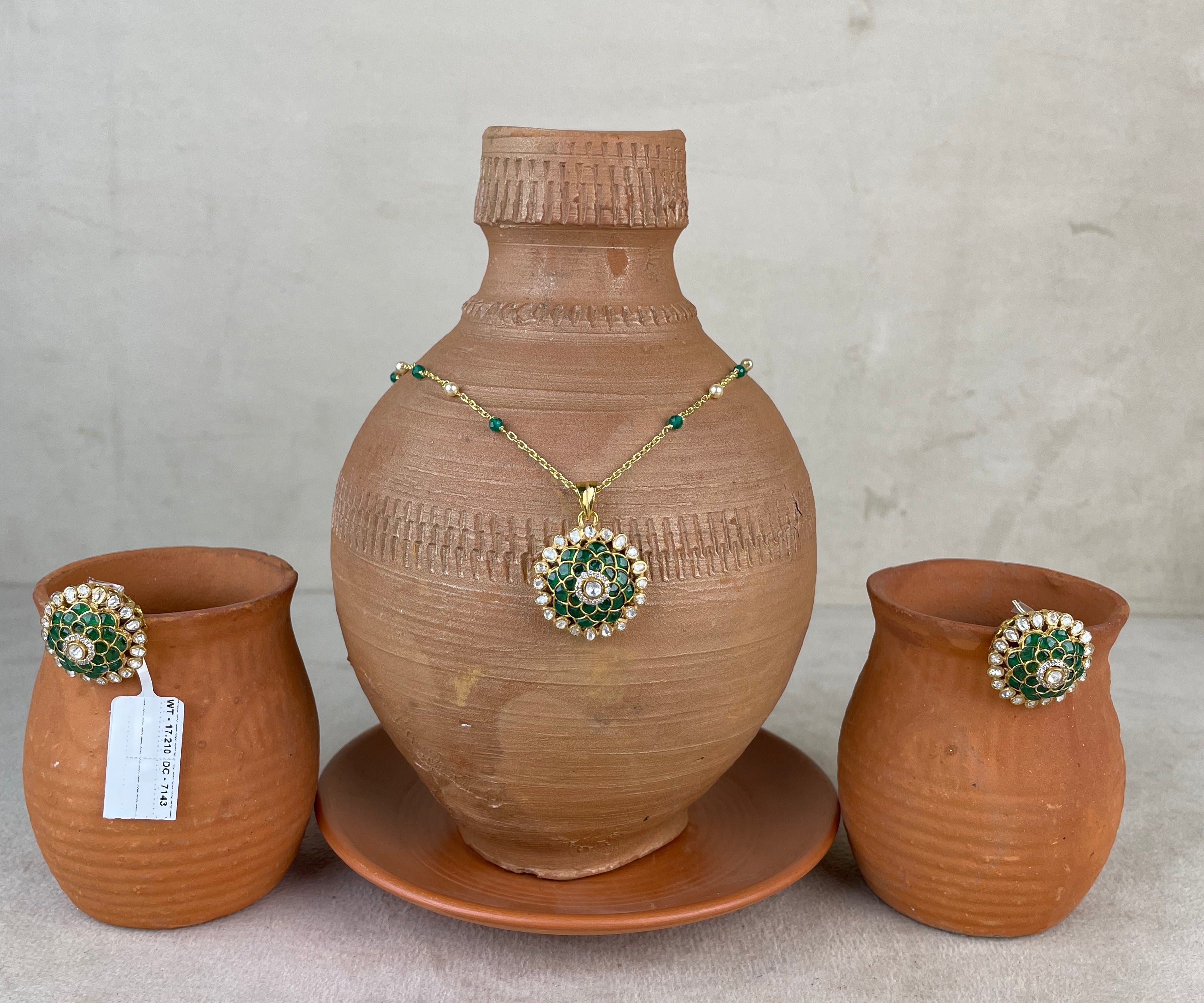 A terracotta clay set featuring a large decorative vase on a matching saucer, flanked by two smaller clay pots, with a gold-tone necklace and matching brooch displayed on the vase.