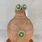 A gold jewelry set featuring a necklace and matching earrings with green and white enamel detailing, displayed on a terracotta vase against a neutral background.