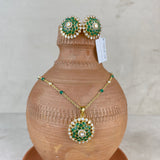 A gold jewelry set featuring a necklace and matching earrings with green and white enamel detailing, displayed on a terracotta vase against a neutral background.