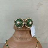 A pair of ornate green and gold floral stud earrings with pearl-like accents, displayed on a terracotta jewelry bust alongside a matching green and gold necklace against a neutral light gray background.