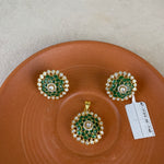 A jewelry set featuring a gold pendant and matching earrings with green enamel floral detailing and white stones, displayed on a terracotta-colored ceramic plate against a neutral background.