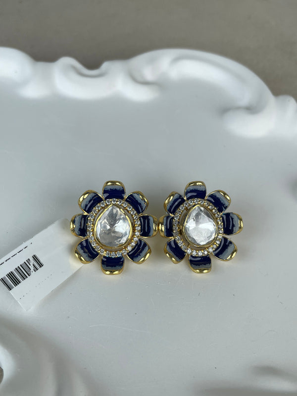 A pair of gold and navy blue flower-shaped earrings with clear teardrop center stones, resting on a white decorative tray.