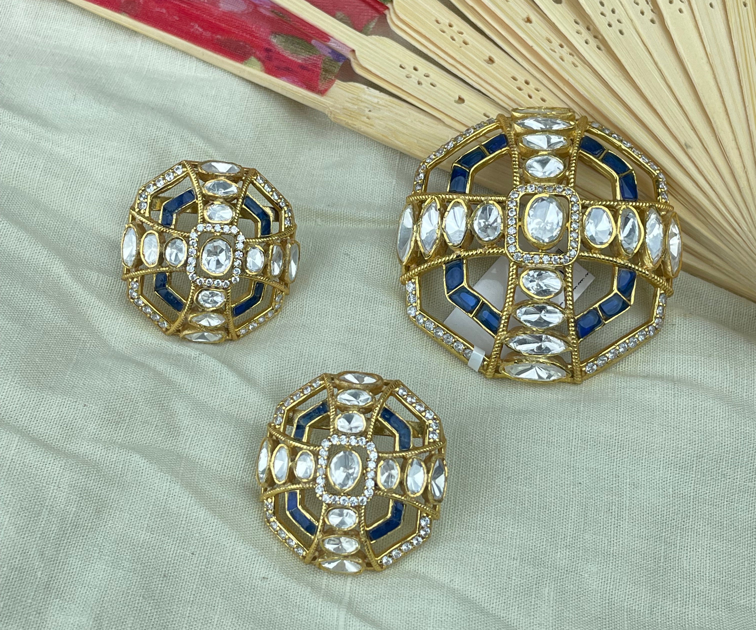 Pendant Set jewelry pieces with blue and white inlay, displayed on a light beige fabric background with a decorative folding fan in the upper right.