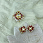 Pendant Set with matching a pair of gold-toned floral stud earrings with red stones and a central clear stone, displayed on a pale fabric surface with a matching larger decorative piece above.