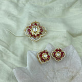 Pendant Set with matching a pair of gold-toned floral stud earrings with red stones and a central clear stone, displayed on a pale fabric surface with a matching larger decorative piece above.