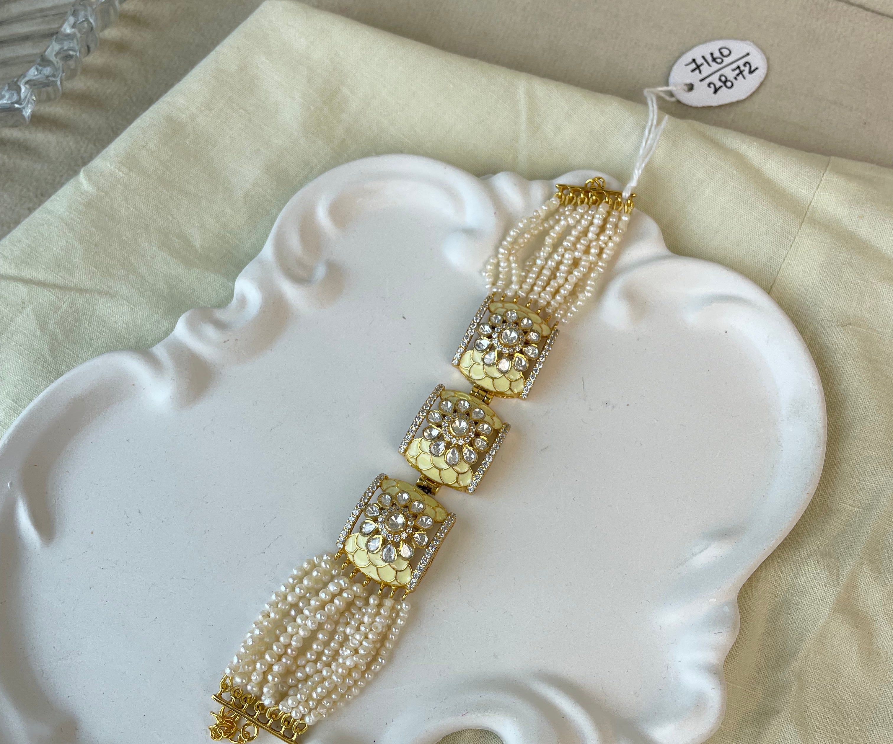 A gold and white beaded traditional jewelry accessory with ornate gold-toned decorative elements, displayed on a white decorative tray over a cream fabric surface.