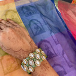 A close-up of a person's decorated wrist wearing a wide, multi-strand statement bracelet, resting over a colorful printed fabric.
