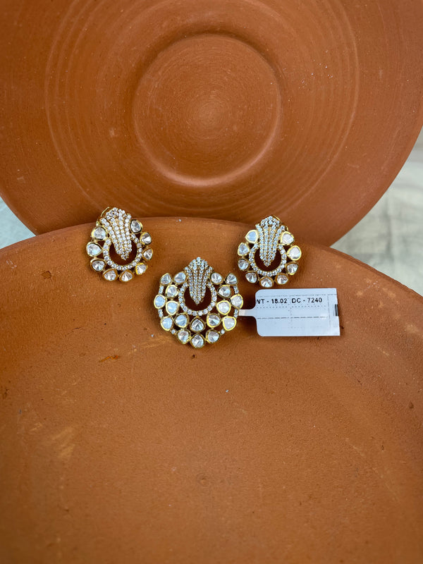 Three ornate gold-toned pendant and earrings with clear rhinestones and dark red enamel details, arranged on a terracotta-colored ceramic surface with a small white inventory tag.