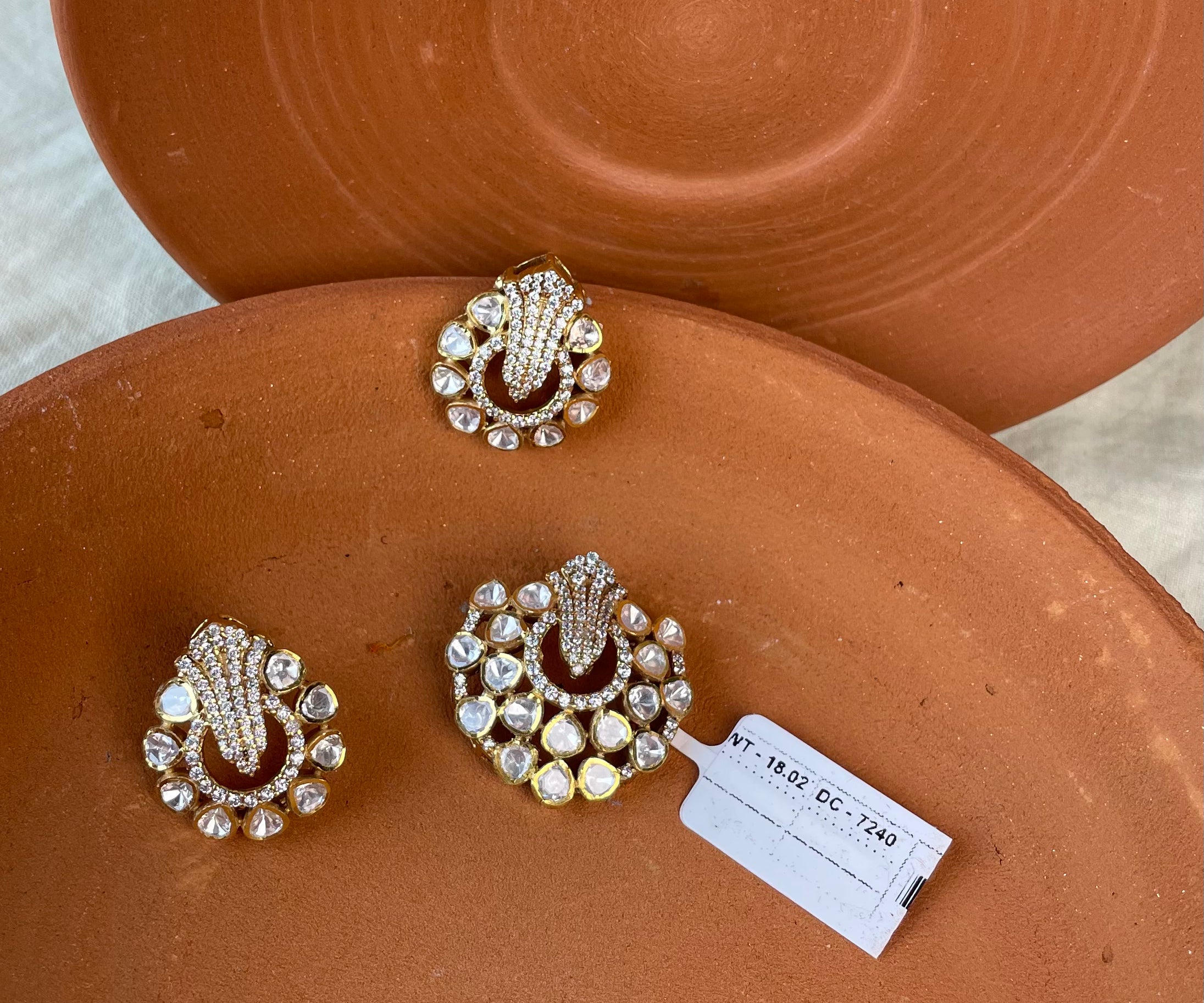 Three ornate gold-toned pendant set with clear rhinestones and deep red enamel details, displayed on terracotta plates with a small white inventory tag.