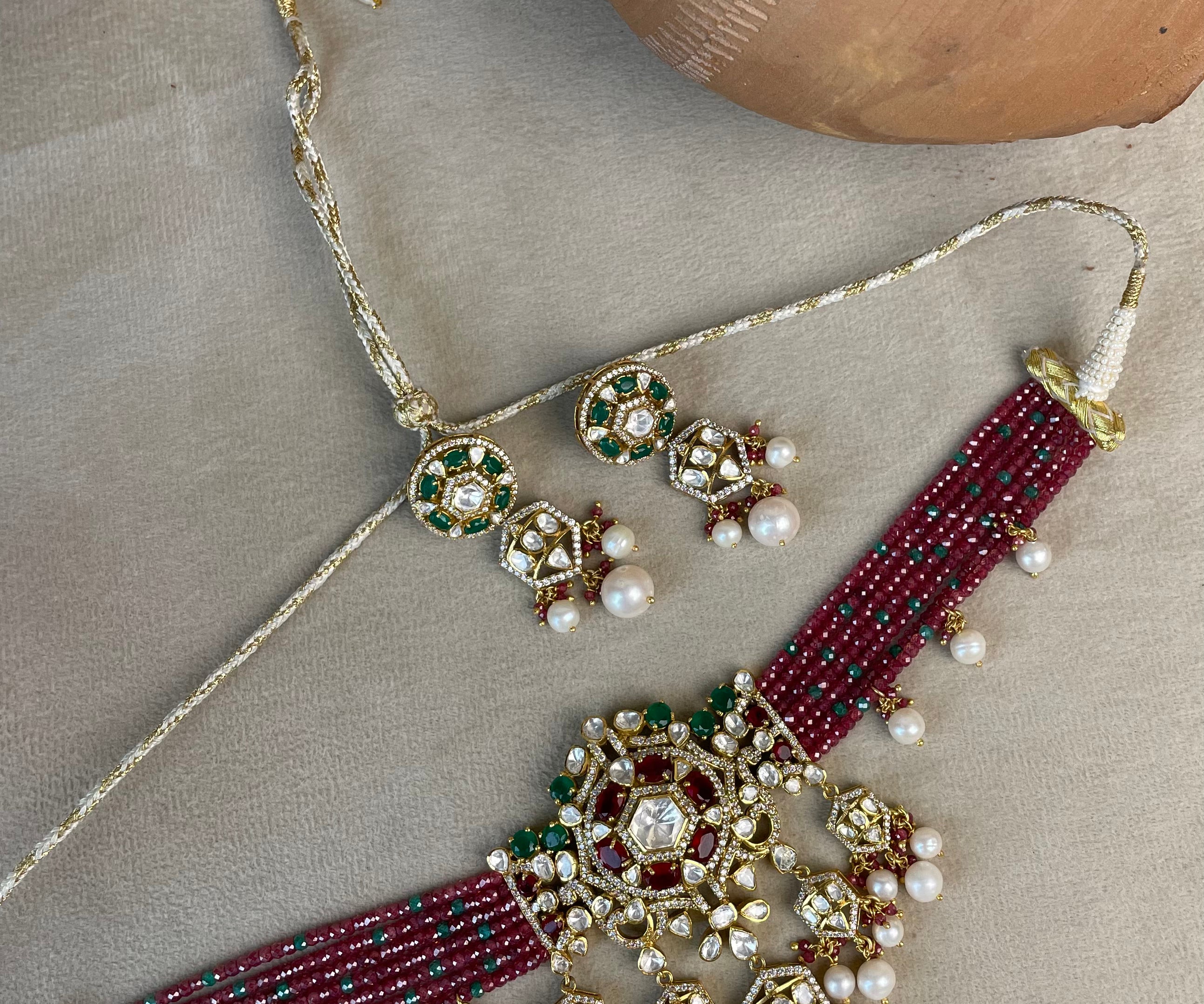 An ornate traditional Indian jewelry set featuring a beaded necklace, matching earrings, and a waist chain laid out on a neutral fabric background with clay pots.