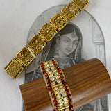 Gold-plated filigree bangles with red gemstone accents, displayed on a wooden stand in front of a vintage-style illustration of a woman.