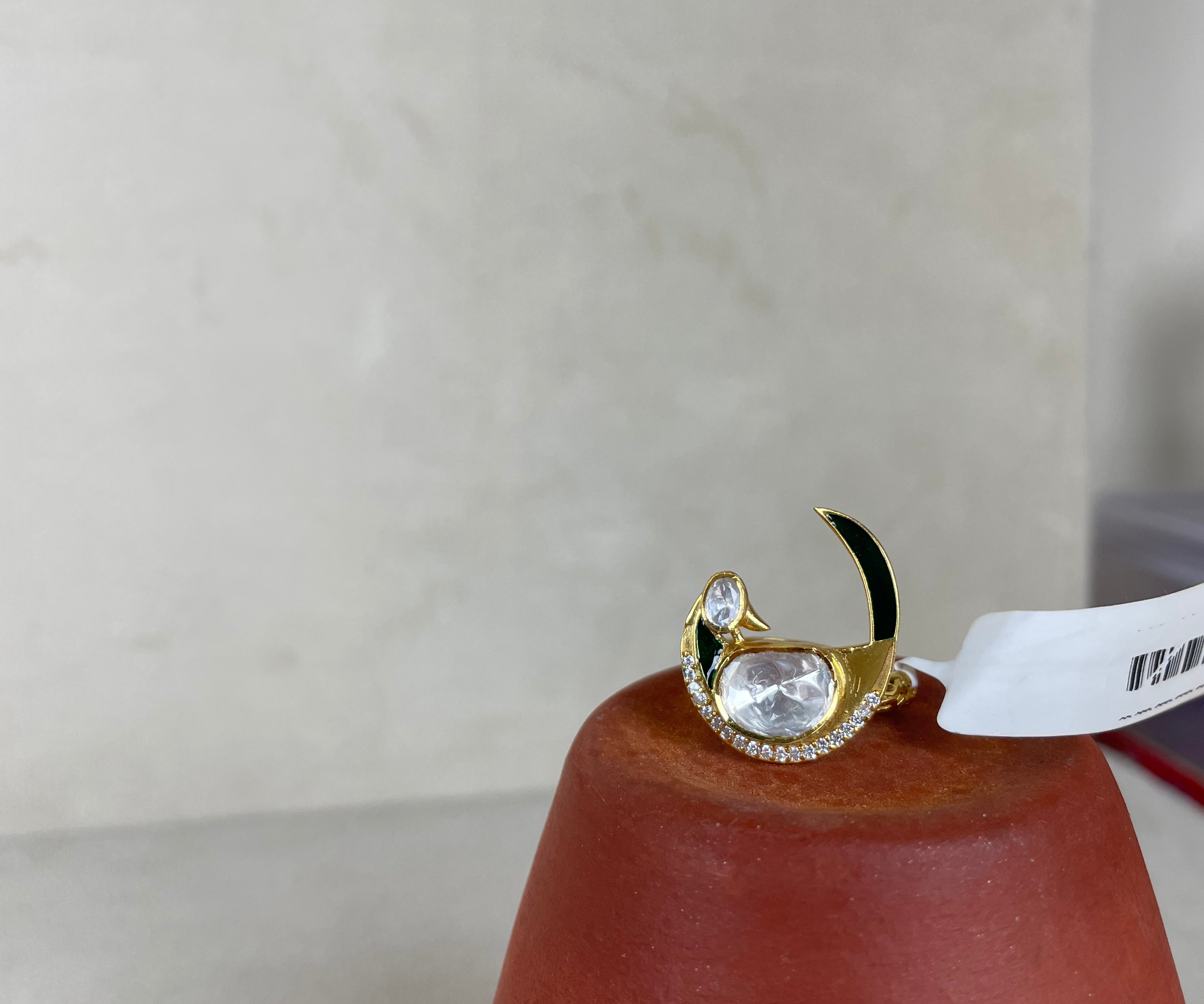 A gold crescent moon ring with a large clear oval gemstone and small clear stones, displayed on a terracotta cone against a light beige background.
