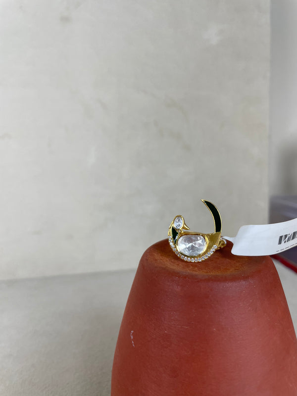 A gold crescent moon ring with a large clear oval gemstone and small clear stones, displayed on a terracotta cone against a light beige background.