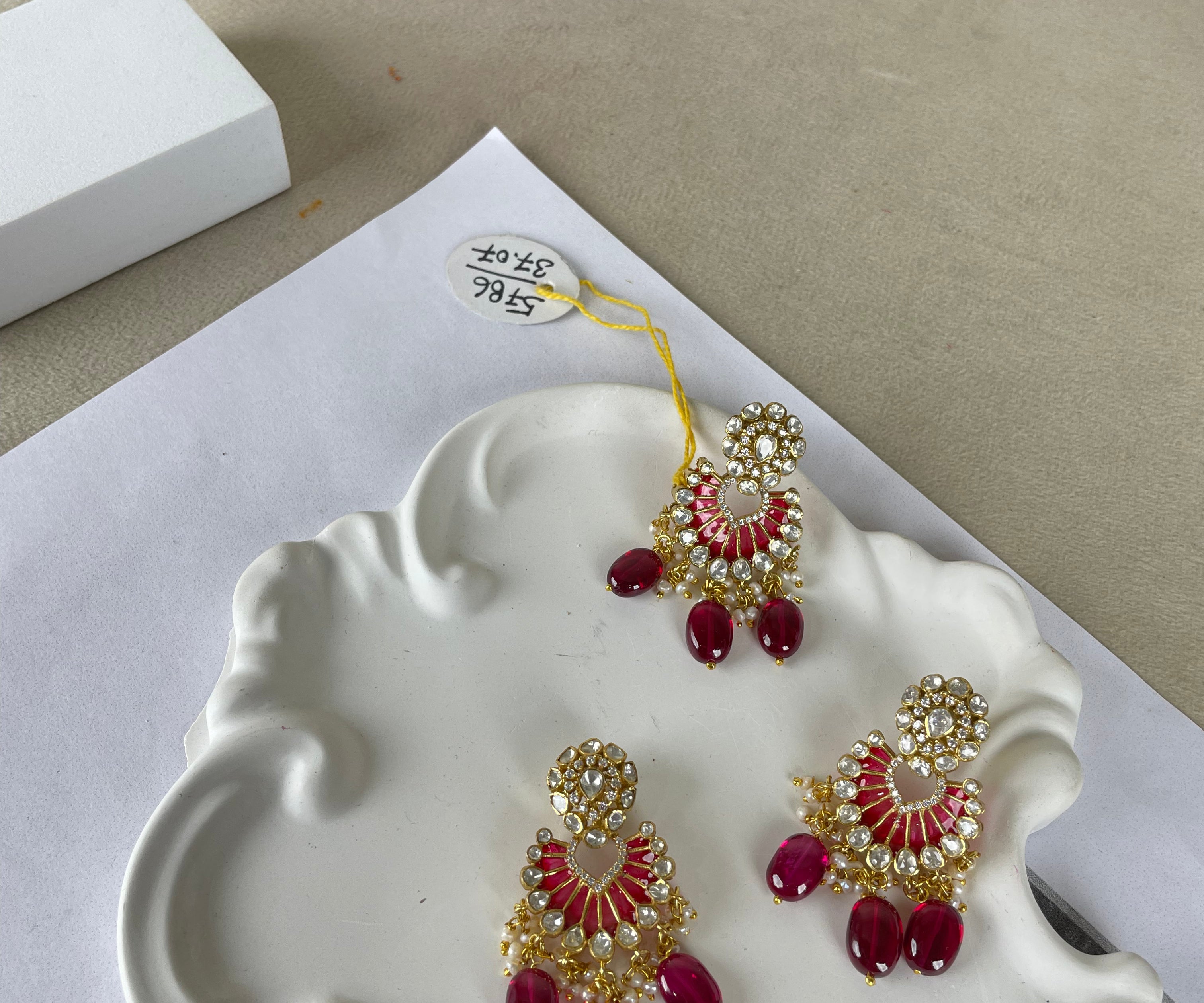 Three pairs of traditional Indian jhumka earrings with red stones and gold-plated settings, displayed on a white decorative tray.